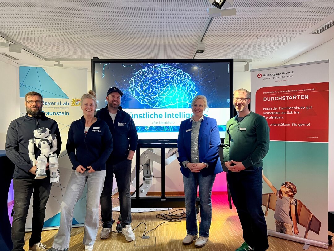 Links 3 Mitglieder vom BayernLab Traunstein und rechts zwei von der Agentur für Arbeit vor einem großen Bildschirm mit dem Schriftzug Künstliche Intelligenz